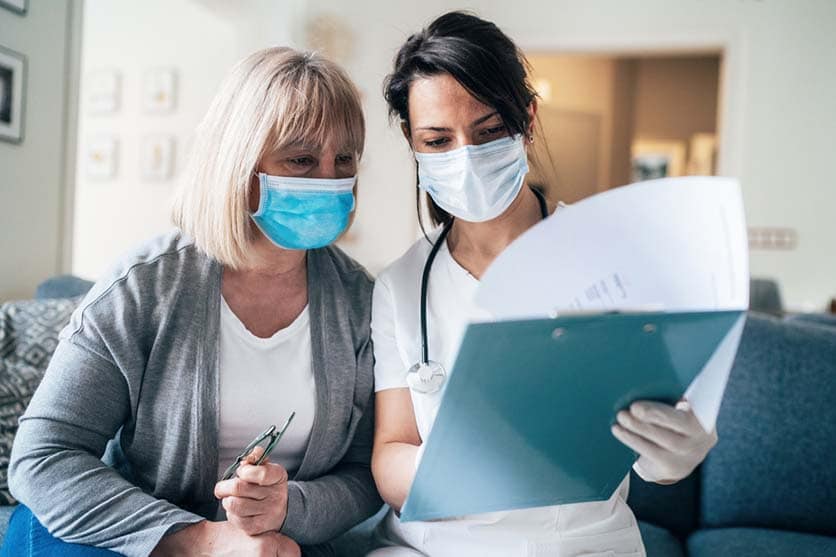 Ärztin und Patientin mit Maske schauen auf ein Datenblatt
